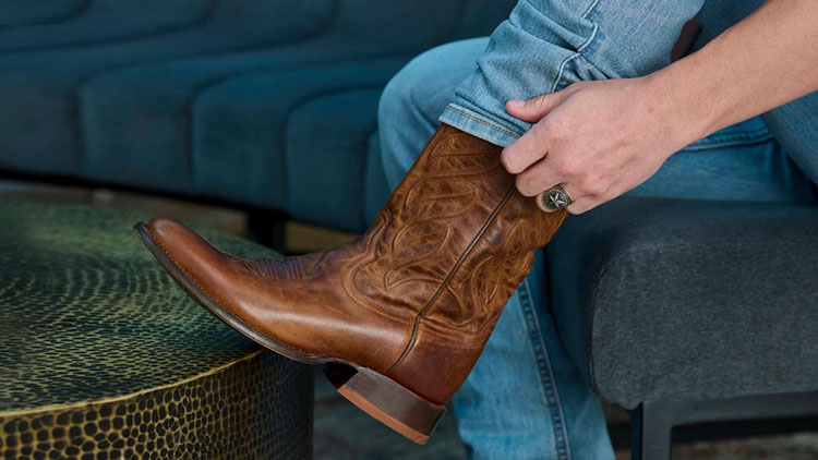 A man with his foot on a table putting on a pair of Tony Lama boots.